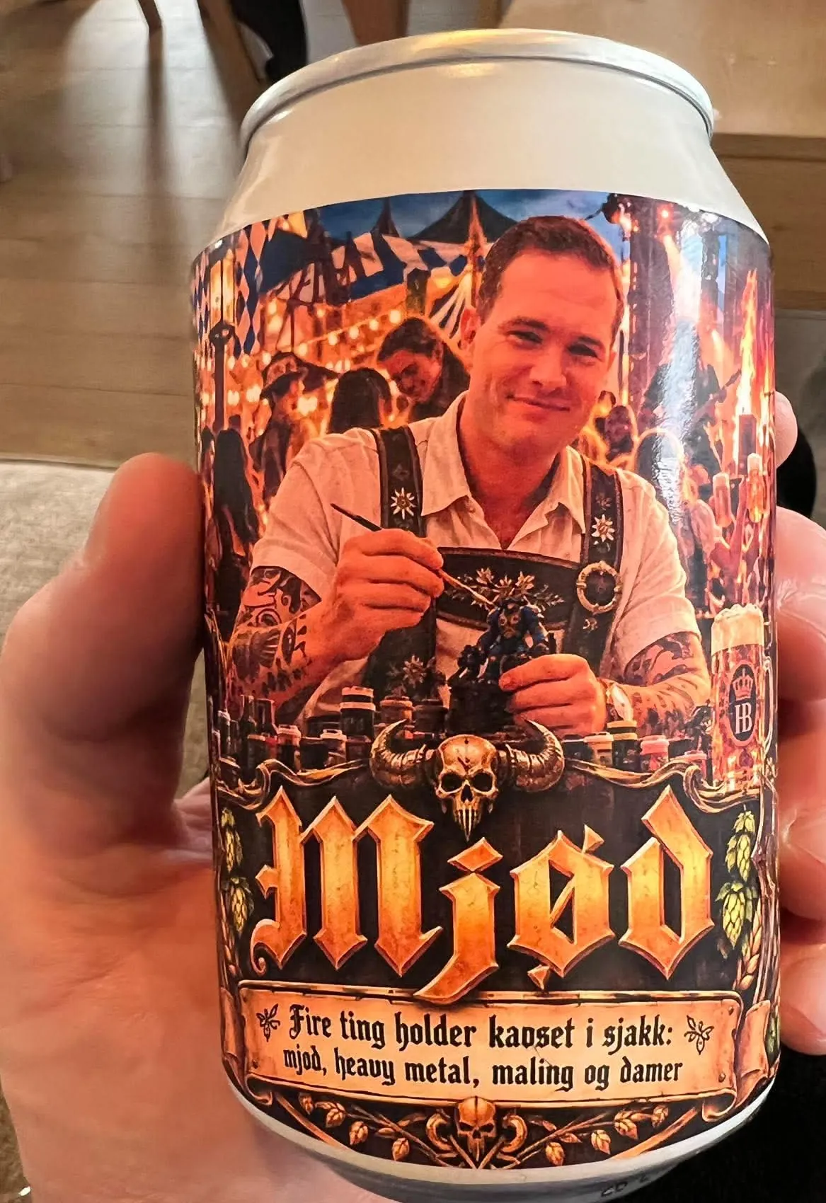 Ølboks med etiketten «Mjød» holdt i hånden, med portrett fra festteltet og et slagord nederst