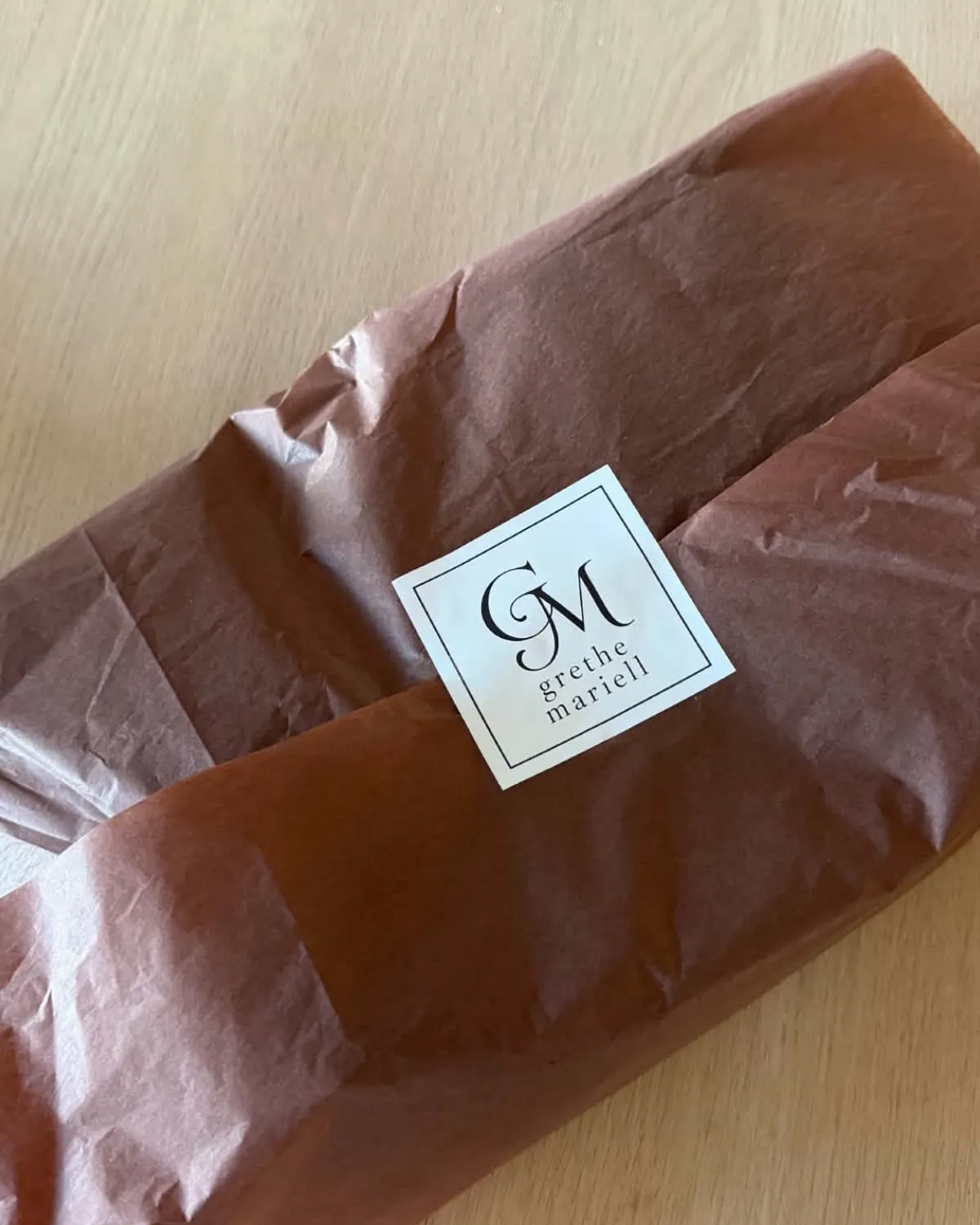 Nærbilde av en pakke i silkepapir som holdes sammen av en hvit kvadratisk sticker med monogrammet GM